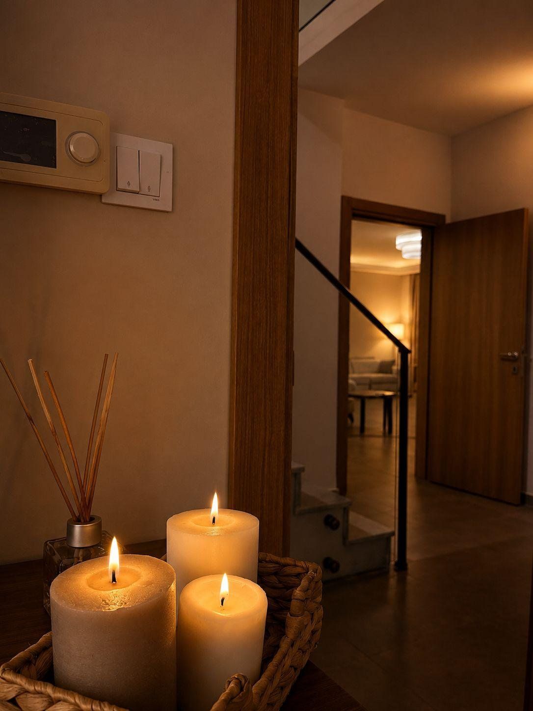 A hallway with a wooden floor, a wall-mounted light switch, and a door leading to another room.