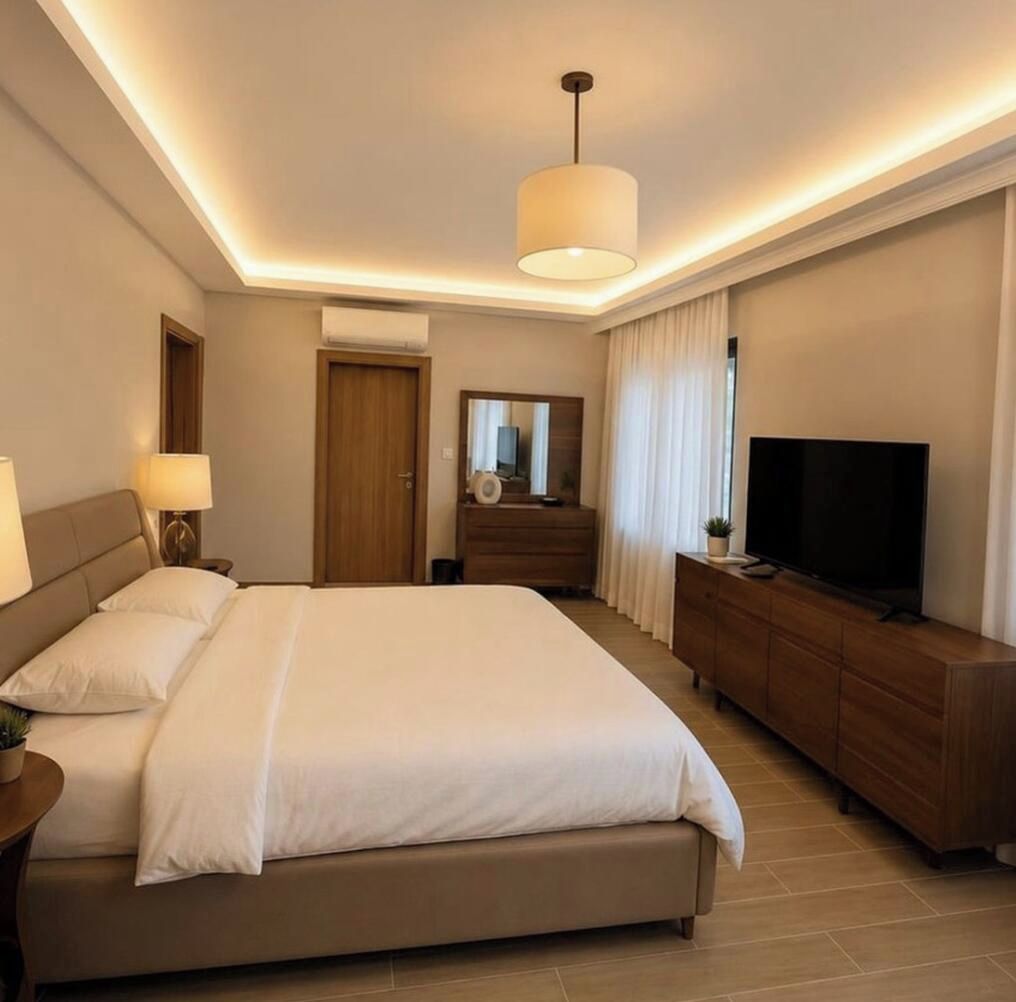 Une chambre d’hôtel comprenant un lit, des lampes de chevet, une commode, un téléviseur et un luminaire au plafond.