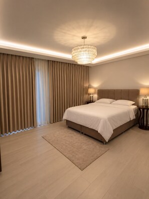 A modern bedroom with a large bed, a chandelier, and a view of the outdoors through curtains.