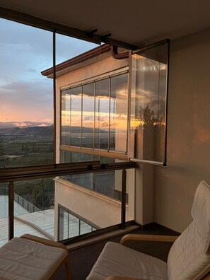 A balcony with a view of a sunset over a valley, a chair, and a table.