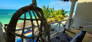 A beach view from a room with a rope chair, a thatched roof, and a patterned floor. - Mrembo Bay Hotel (Jambiani)