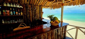A beachside bar with a wooden counter, a thatched roof, and a view of the ocean. - Mrembo Bay Hotel (Jambiani)