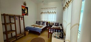 Una habitación con dos camas, un estante de madera, una mesita pequeña y una ventana con cortinas.