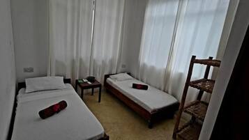 Una habitación con dos camas individuales, una mesita y una silla.