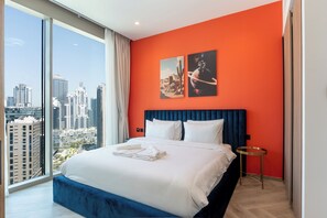 Ein Hotelzimmer mit einem großen Bett, Blick auf die Stadt und zwei gerahmten Bildern an der Wand.