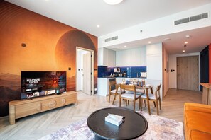 Ein modernes Wohnzimmer mit Flachbildfernseher, Holzmöbeln, einer Essecke und einer Küche.