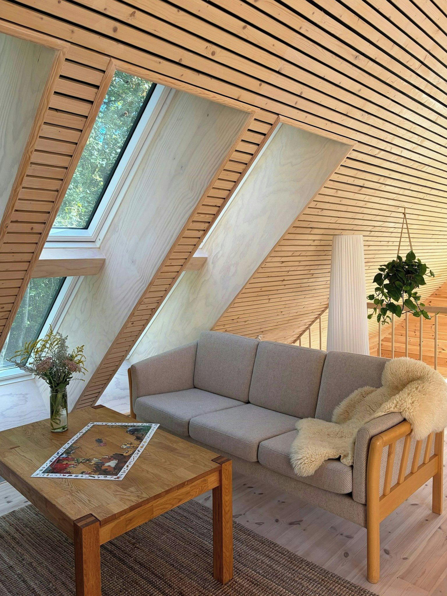 Una stanza accogliente con soffitto spiovente, un divano, un tavolo con una rivista e una pianta sospesa.