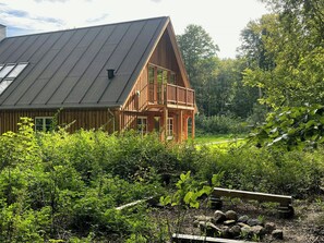 Eine Holzhütte mit geneigtem Dach und einem Balkon, umgeben von dichtem Grün.