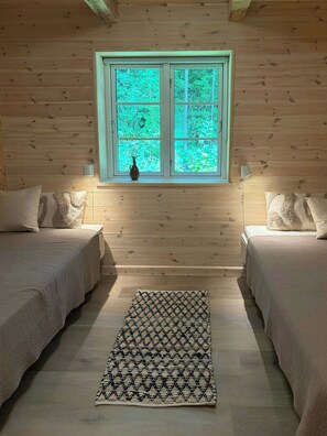 Ein Zimmer mit zwei Betten, einem Fenster mit Blick auf Bäume und einem gemusterten Teppich auf dem Boden.