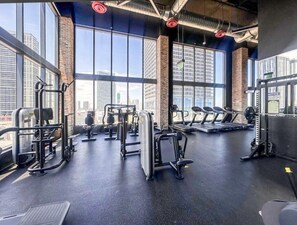 Une salle de sport équipée de divers appareils d’exercice, dotée de grandes fenêtres et offrant une vue sur la ville.