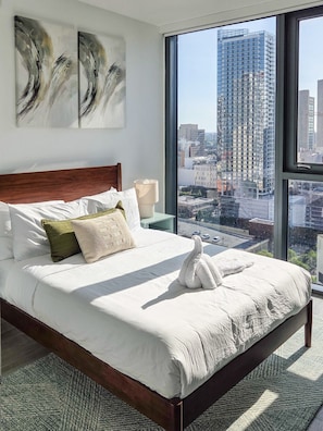 A hotel room with a large bed, a nightstand, a lamp, and a view of a cityscape through a large window. - Luxury Apartment with Shared Pool and Skyline View (Miami)
