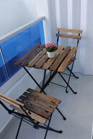 Ein Balkon mit Holztisch und -stühlen, einem Blumentopf und einem blauen Geländer.