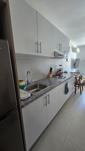 Een moderne keuken met een granieten aanrecht, een roestvrijstalen spoelbak en witte kasten.