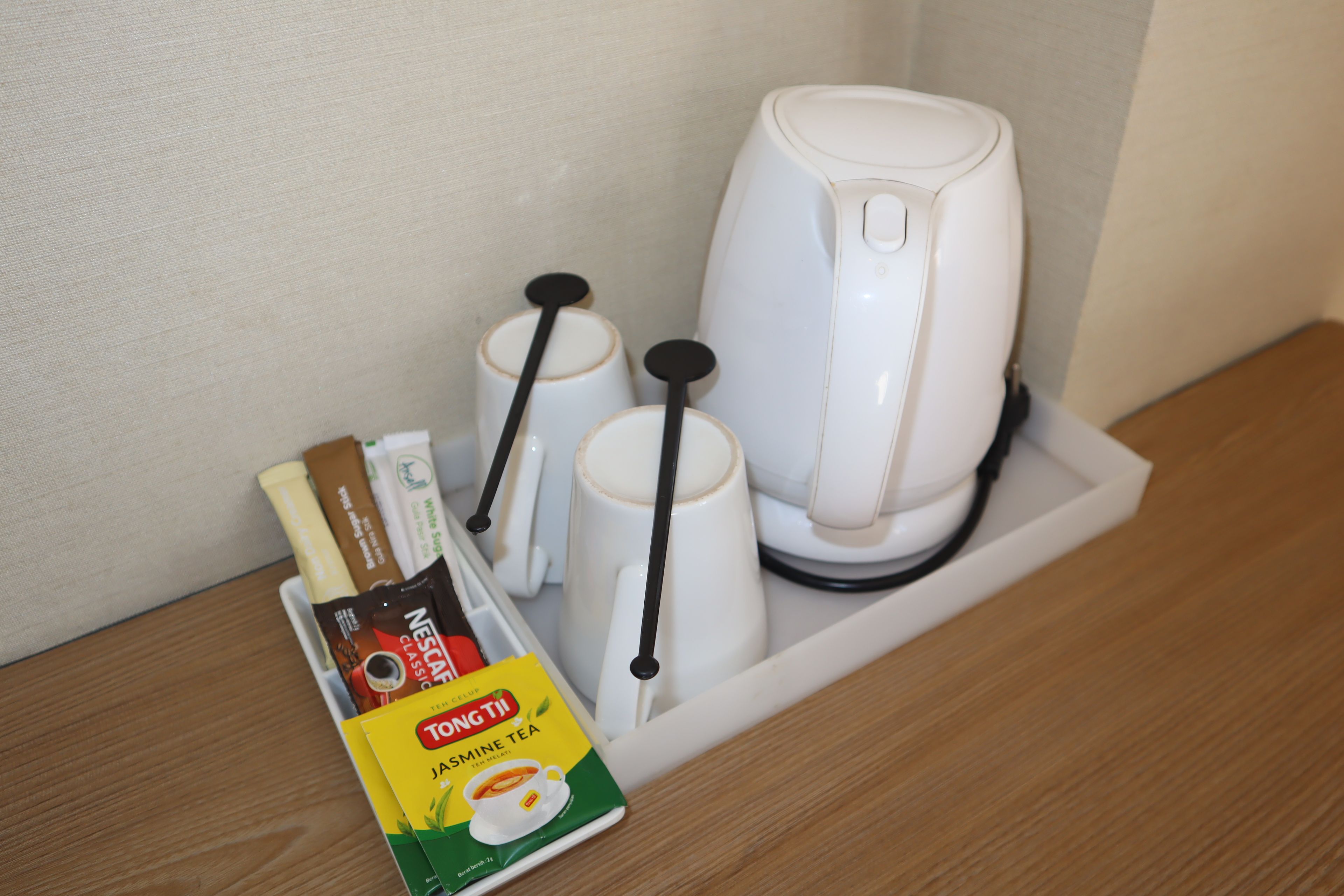 A coffee maker, two cups, and a box of Tongtong Jasmine Tea on a wooden surface.