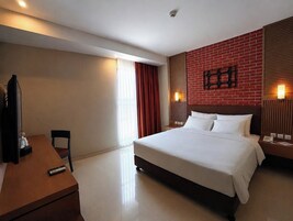 Una habitación de hotel con cama, escritorio, silla, televisor y una pared de ladrillo rojo.