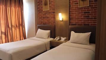 A hotel room with two beds, a brick wall, a mirror, and a nightstand with a phone.