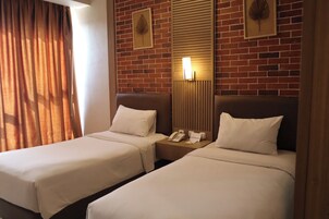 Habitación de hotel con dos camas, una pared de ladrillo, un espejo y una mesita de noche con un teléfono.