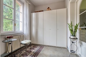 A room with a large white wardrobe, a small table with a bench, a radiator, and a potted plant. - GuestHost - The Little Tower Between Heaven and Earth (Perugia)