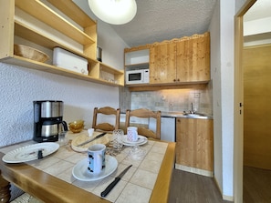 A compact kitchen with wooden cabinets, a microwave, and a coffee maker. - (BO.130) Family-friendly two-bedroom apartment with a view of the slopes, Les Menuires (Les Menuires)