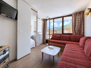 A modern living room with a red sofa, a white coffee table, and a television mounted on the wall. - (BO.130) Family-friendly two-bedroom apartment with a view of the slopes, Les Menuires (Les Menuires)