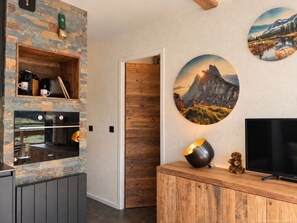A modern kitchen with a stone backsplash, built-in oven, and a wooden cabinet. - (CI.17B) – Alpine Lodge - Premium "Skis on" Package (Les Menuires)