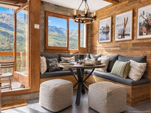 A cozy room with a wooden wall, a large window, a dining table, and a seating area. - (CI.17B) – Alpine Lodge - Premium "Skis on" Package (Les Menuires)