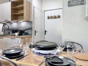 Una cocina moderna con una mesa de comedor preparada para dos personas, equipada con una hornilla portátil, diferentes utensilios de cocina y cristalería.