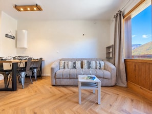 Ein Wohnzimmer mit einer Couch, einem Esstisch mit Stühlen, einem kleinen Couchtisch und einem Fenster mit Vorhängen.