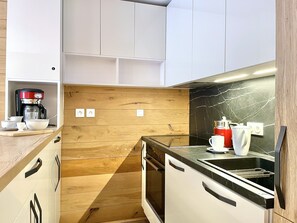 A compact kitchen with white cabinets, a wooden backsplash, and a black countertop. - (VM.308) 4-room PREMIUM - Alpine Style - (Les Menuires)