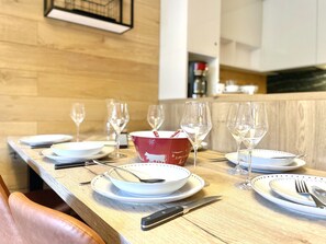Taula de dinar preparada amb plats, coberts i vasos de vi, amb un bol vermell al centre.