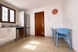 Eine Küche mit Kühlschrank, Geschirrspüler und Schränken. Eine Holztür und eine Uhr sind an der Wand zu sehen.