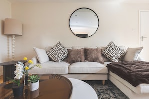 Un salon avec un canapé, un miroir rond, une lampe et une table basse ornée de fleurs.