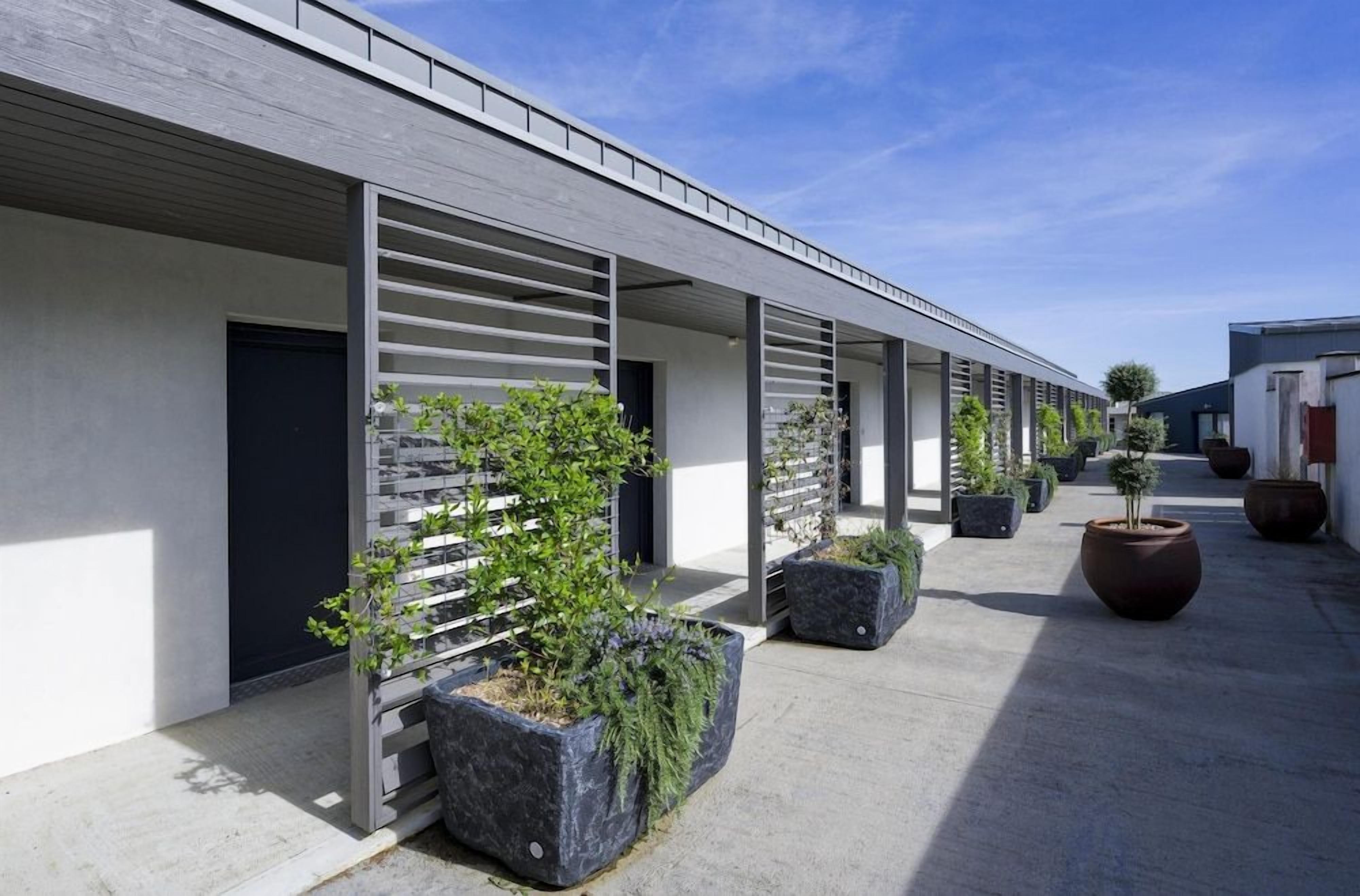 A modern building with a covered outdoor area, potted plants, and a clear sky.