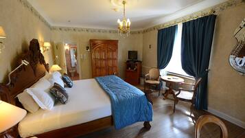 A hotel room with a large bed, a desk, a chair, a television, and a window with curtains.