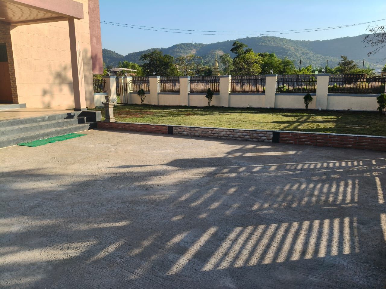 Un área pavimentada con un edificio a la izquierda, una cerca y vistas a una colina con árboles.