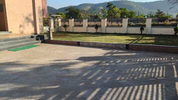 Un área pavimentada con un edificio a la izquierda, una cerca y vistas a una colina con árboles.