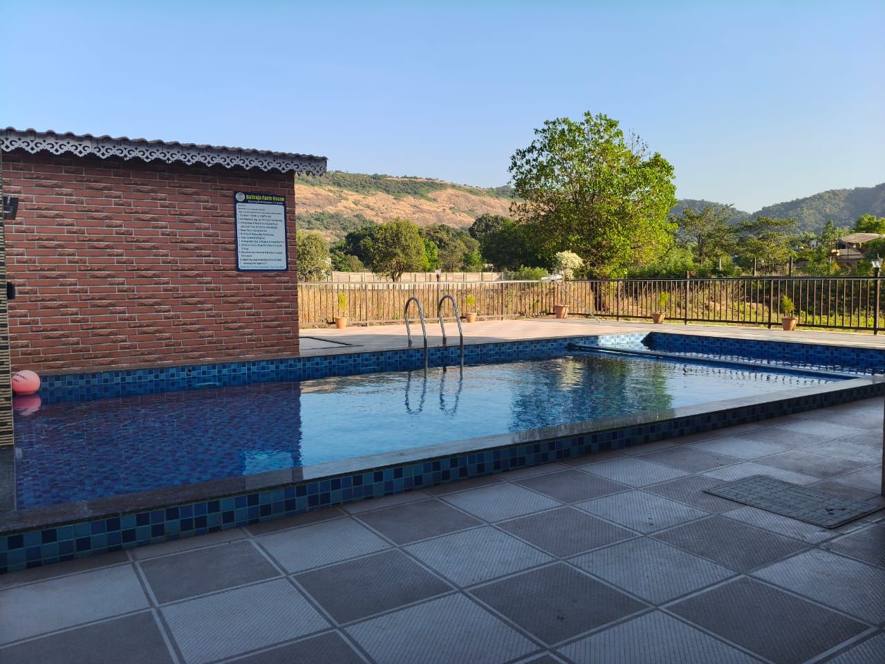 A swimming pool with a tiled edge, a brick structure with a sign, and a view of hills in the background.