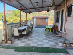 Une terrasse extérieure dotée d’un espace salon abrité, d’un petit bâtiment en briques et de plantes en pot.