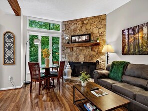 A living room with a stone fireplace, wooden furniture, and a large window. - Laurelwood 64 with Wintergreen Advantage (Wintergreen)