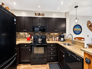 Une cuisine moderne avec des meubles de rangement aux couleurs sombres, un réfrigérateur noir, un four à micro-ondes, une cuisinière et un lave-vaisselle.