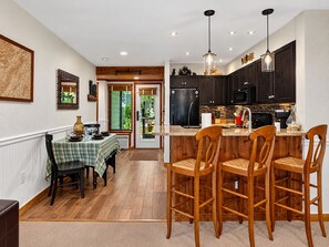 A modern kitchen with dark cabinets, a central island with bar stools, and a dining area with a checkered tablecloth. - Dobie 25 with Wintergreen Advantage (Wintergreen)
