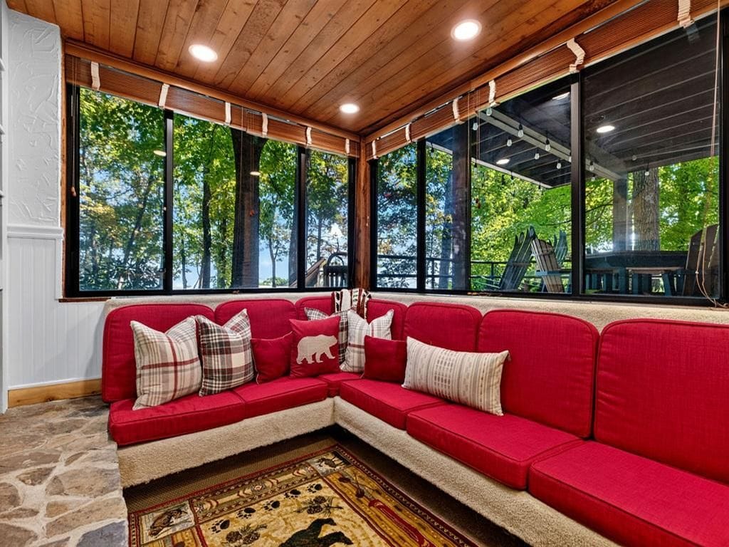 A red sectional sofa with patterned cushions, a stone floor, and large windows with a view of trees.