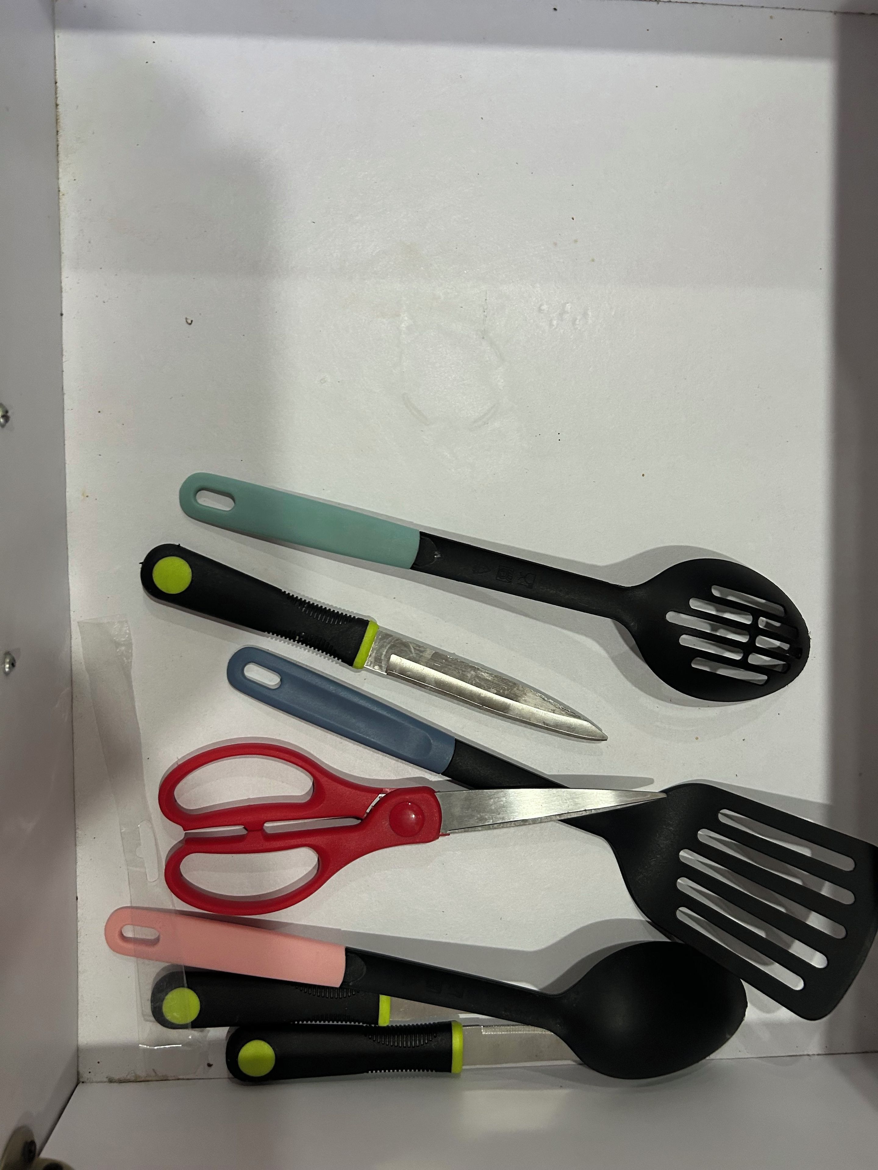 A drawer containing various kitchen utensils including a spatula, scissors, and a spoon.