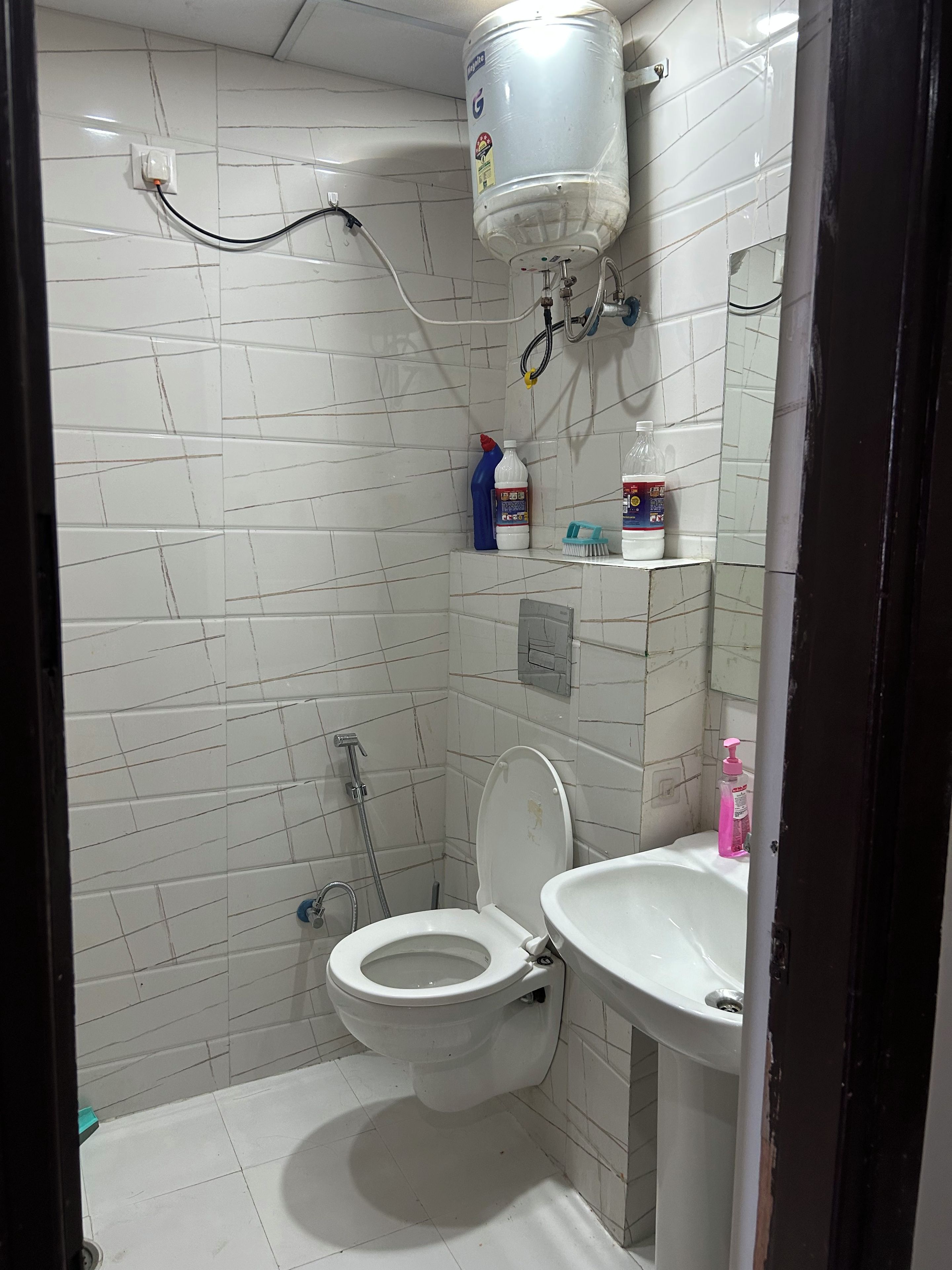 Ein kleines Badezimmer mit Toilette, Waschbecken und einem an der Wand montierten Warmwasserbereiter.