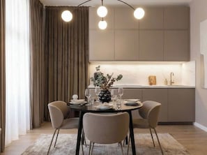 Un espace repas moderne avec une table ronde, quatre chaises, un vase agrémenté de plantes et une cuisine en arrière-plan.