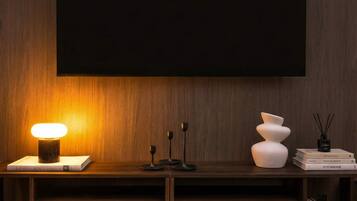 Ein modernes Wohnzimmer mit einem dunklen Holz-TV-Möbel, einer beleuchteten Tischlampe und einem flachbildfernseher, der an der Wand angebracht ist.