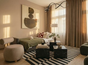 A modern hotel room with a bed, a seating area with ottomans, a coffee table, and a large abstract painting on the wall. - TurnKey | Top-Floor 2BR for 12, Central Prague (Praha 2)
