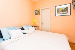 A bedroom with a bed, pillows, a nightstand, a lamp, and two framed pictures on the wall. - Apartment Vukoja - One-bedroom Apartment With Balcony (Dubrovnik)