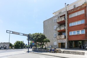A street view with a stop sign, a pedestrian crossing, and a building with multiple floors and balconies. - Apartment Vukoja - One-bedroom Apartment With Balcony (Dubrovnik)