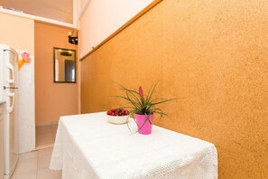 A room with a white table, a pink pot with a plant, and a bowl of cherries. - Apartment Vukoja - One-bedroom Apartment With Balcony (Dubrovnik)